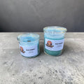 Two blue raspberry candles in glass jars on a concrete surface with a gray background.